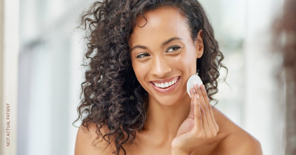 female (model) with glowing skin cleansing her face with a cotton round